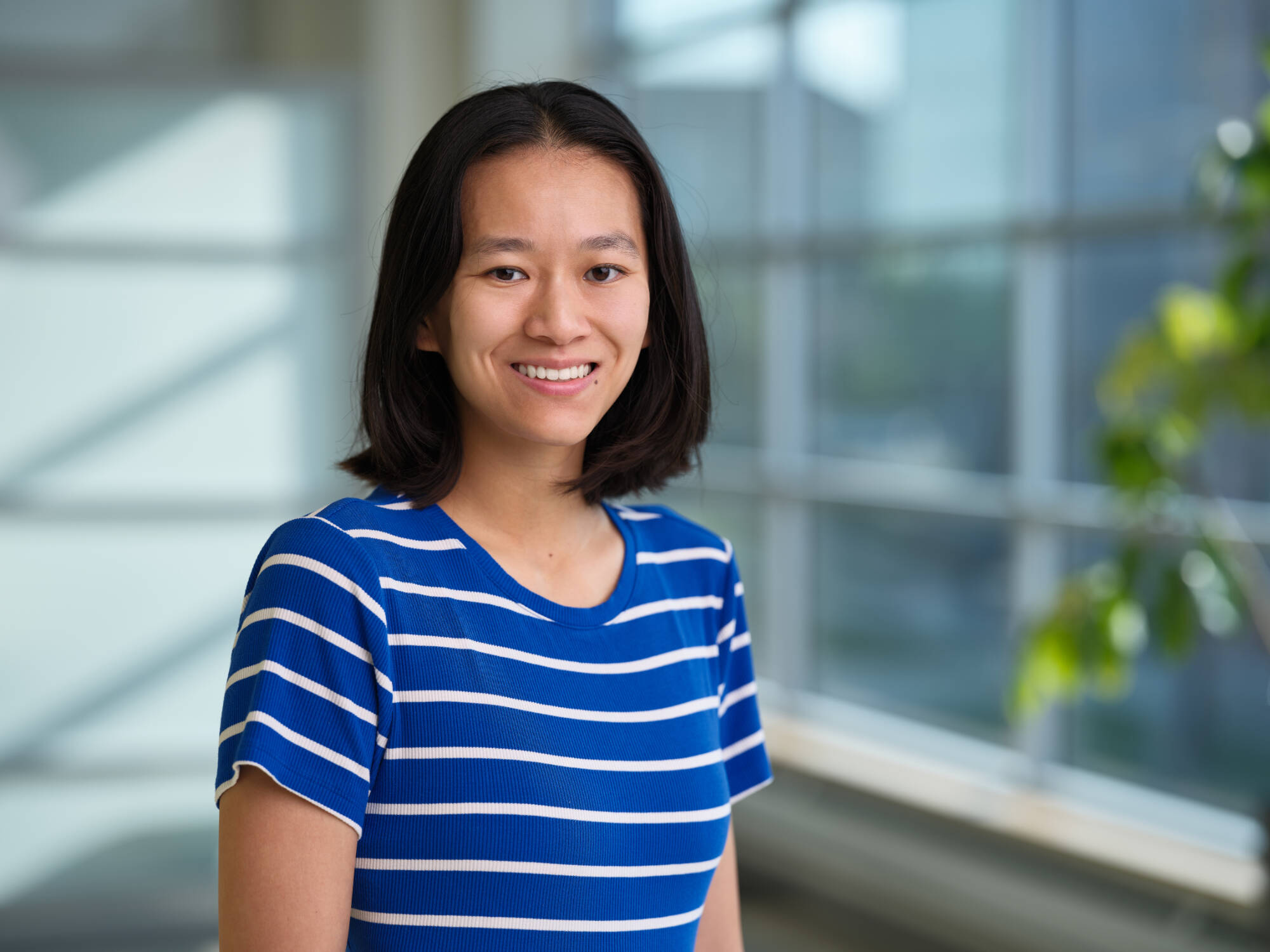 An individual smiling at the camera with a window in the background.